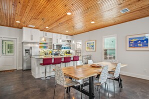 A modern kitchen with white cabinets, a stainless steel refrigerator, and a wooden island with bar stools. - Next to Pool! Boardwalk to the Beach, Happy Ours awaits you! (Port Aransas)