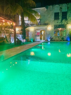 Un hotel con zona de piscina, un cartel que indica el nombre del hotel y la entrada del edificio.