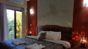 Un lit bien fait, avec une couvre-lit à motifs, une tête de lit en bois et une table de chevet surmontée d’une lampe.