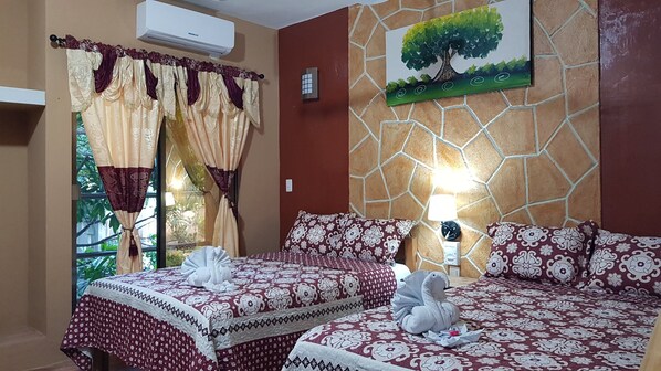 Habitación de hotel con dos camas, un cuadro de un árbol, una pared de piedra y un equipo de aire acondicionado.