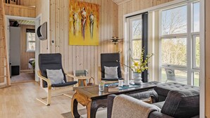 A cozy living room with wooden walls, a large window, two black chairs, a wooden coffee table, and a painting on the wall. - 3 bedroom gorgeous home in Storvorde (Storvorde)