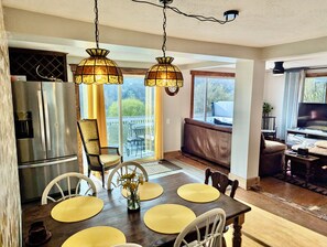 Une cuisine moderne avec un réfrigérateur en acier inoxydable, une table à manger agrémentée de sets de table jaunes et une grande fenêtre donnant sur une terrasse.