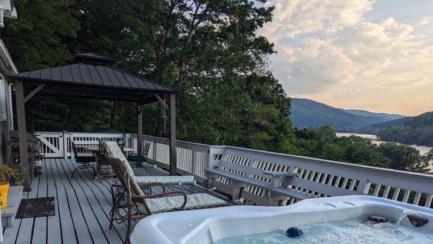A hot tub on a wooden deck with a view of a river and mountains.