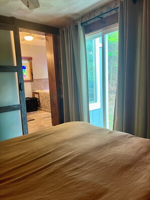 Une chambre à coucher avec un lit, une fenêtre avec des rideaux, une porte et une vue sur l’extérieur.