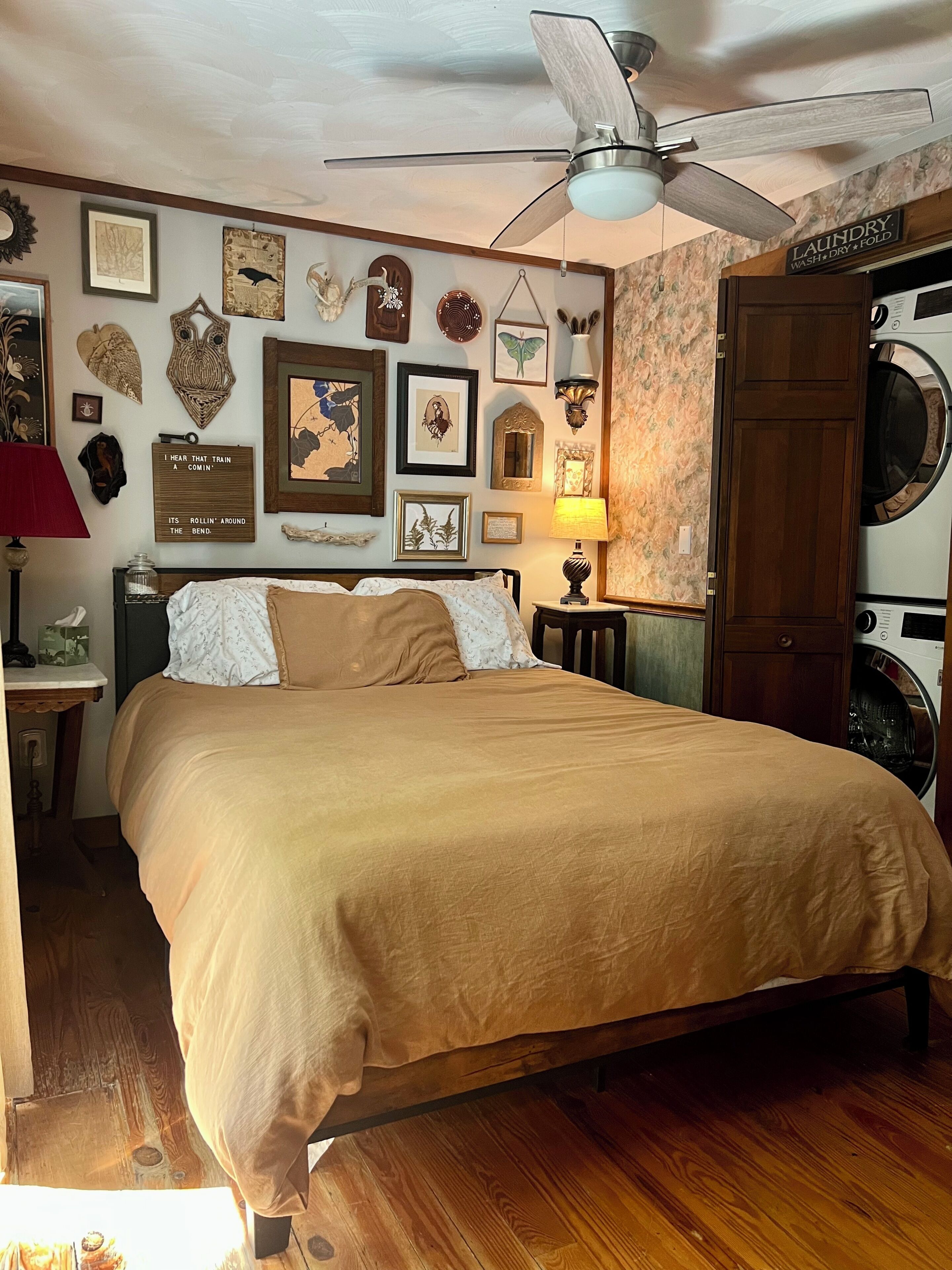 Un dormitorio con cama, ventilador de techo, lámpara de pared y zona de lavandería con lavadora.