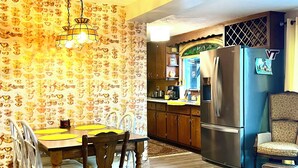 Ein Essbereich mit Holztisch und -stühlen, einer Wand mit Muster und einer Küche inklusive Kühlschrank und Schränken.