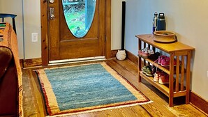 Eine Holztür mit Glasfenster, eine hölzerne Bank, ein kleiner Tisch mit Schuhen und ein an der Wand befestigter Kleiderhaken.