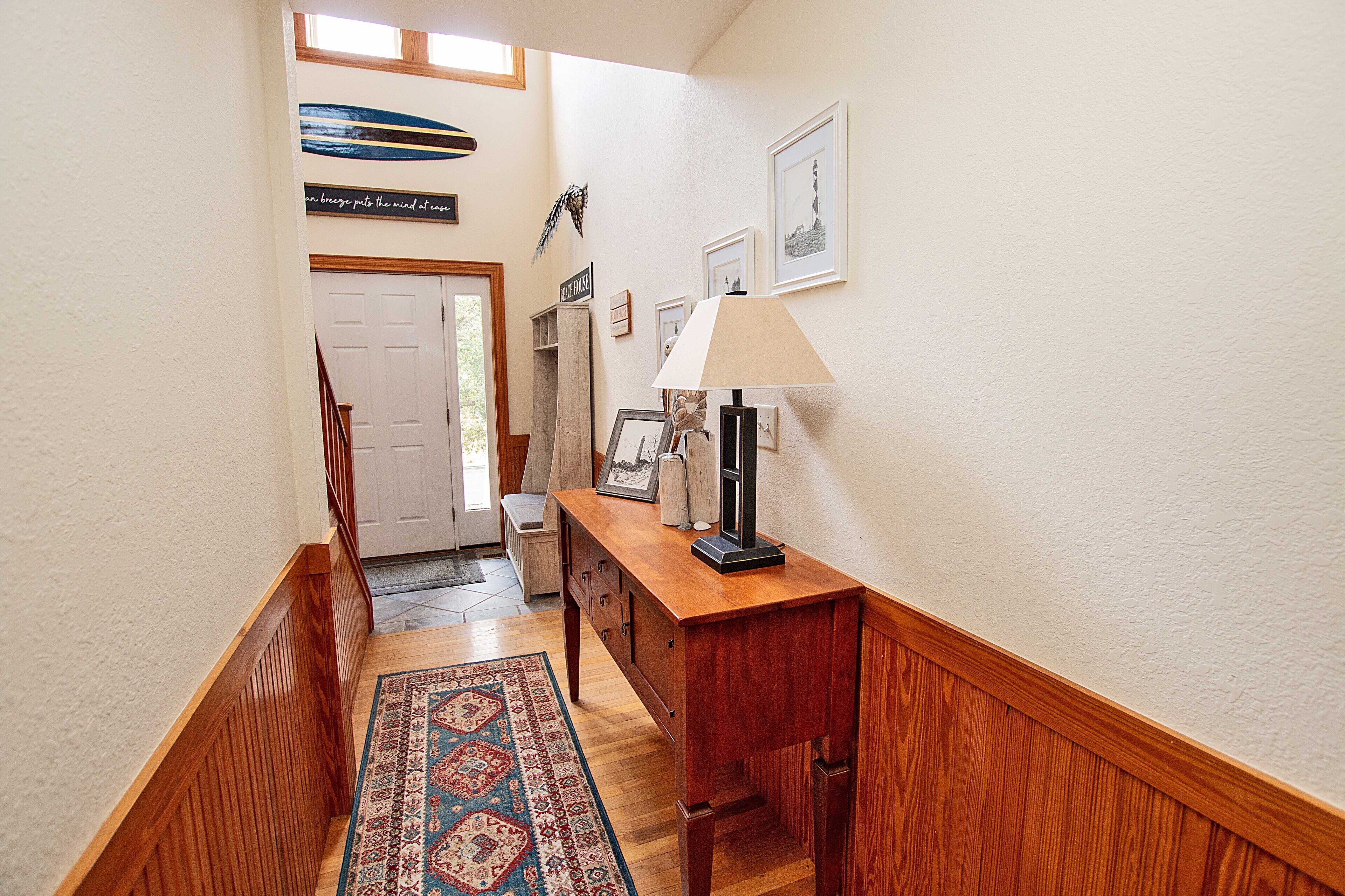 A hallway with a wooden bench, a lamp, and a rug.