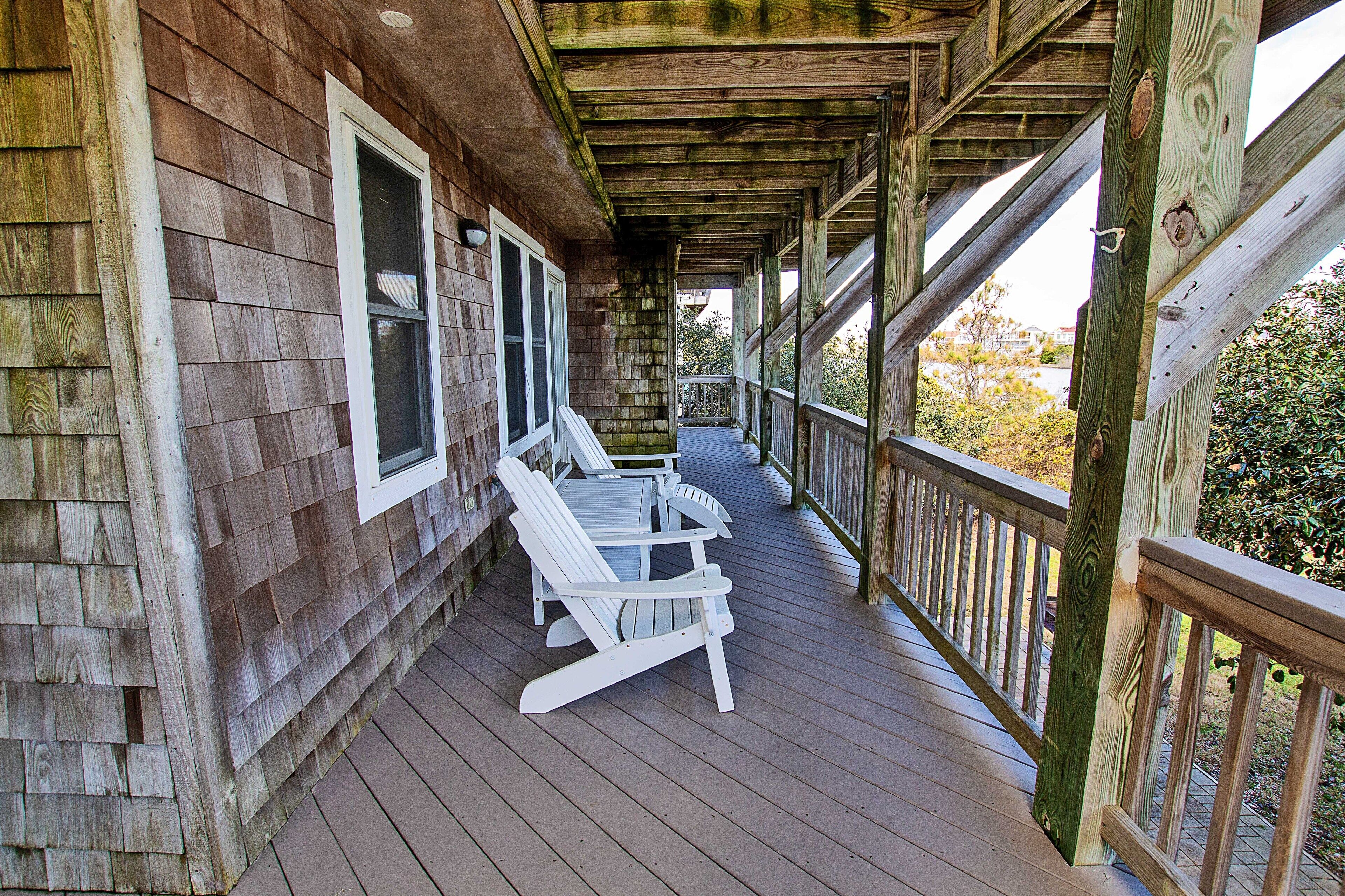 Une terrasse en bois avec une rambarde, une table et deux chaises Adirondack.