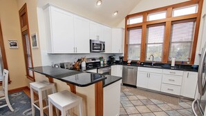 Una cocina con armarios blancos, encimera negra y refrigerador de acero inoxidable.