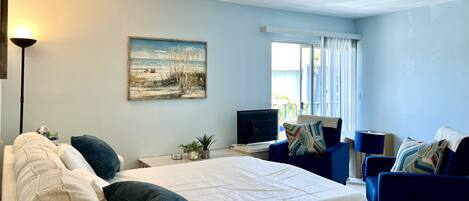 A room with a bed, a desk, a TV, and two blue armchairs.