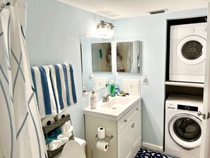 Ein kleines Badezimmer mit Waschmaschine, Waschbecken, Spiegel und Handtuchhalter.