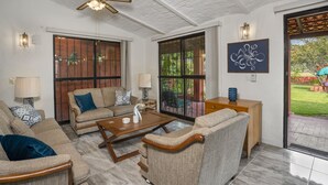 A spacious living room with a ceiling fan, large windows, and a view of the garden.