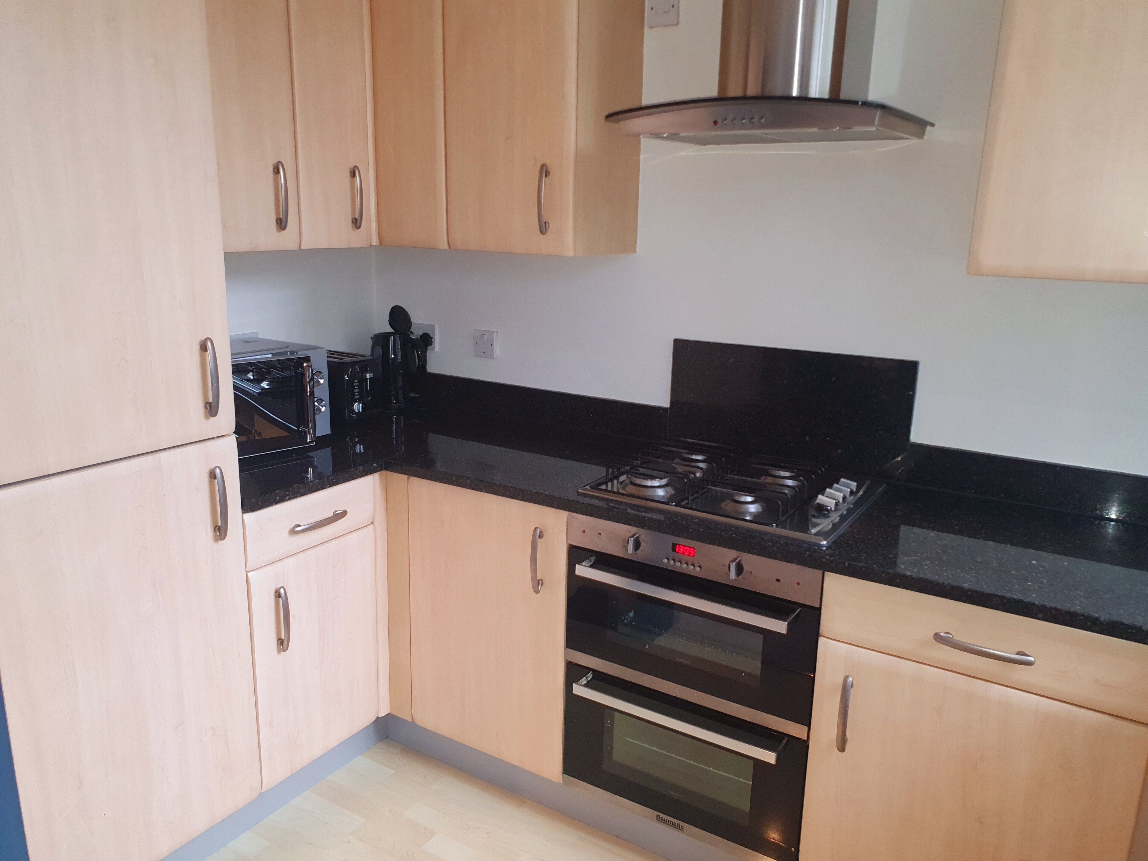 A kitchen with light wooden cabinets, a black countertop, a stove, and an oven.
