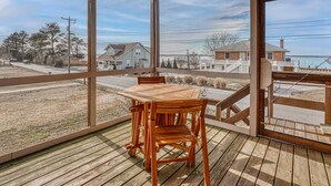 A wooden deck with a table and chairs, overlooking a residential area with houses and a body of water. - Cozy Nest | Water View Retreat w/ Screened Porch, Private Deck Suite & Pet Friendly Comfort for 6 (Chincoteague Island)