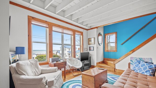 A spacious living room with a large window, a television, and a cozy seating area. - Cozy Nest | Water View Retreat w/ Screened Porch, Private Deck Suite & Pet Friendly Comfort for 6 (Chincoteague Island)