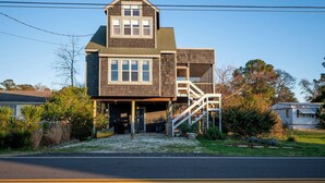 A two-story house with a front porch, a covered garage, and a staircase leading to the upper level. - Cozy Nest | Water View Retreat w/ Screened Porch, Private Deck Suite & Pet Friendly Comfort for 6 (Chincoteague Island)