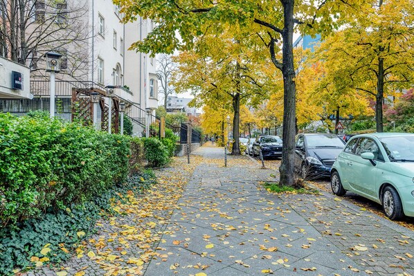 Stroll along a charming urban street lined with trees displaying vibrant autumn foliage and residential buildings with inviting balconies.