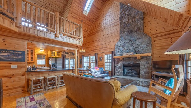 A spacious cabin interior with a stone fireplace, wooden walls, a dining area, and a cozy seating area. - The Great Escape - Cabin with shared pool access and Goshorn Lake access (Saugatuck)