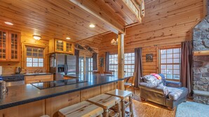 A cabin interior with wooden walls, a stone fireplace, a kitchen with a refrigerator, and a bar area with stools. - The Great Escape - Cabin with shared pool access and Goshorn Lake access (Saugatuck)
