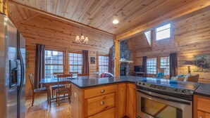 A wooden cabin kitchen with a central island, wooden cabinets, a built-in oven, and a dining area with a table and chairs. - The Great Escape - Cabin with shared pool access and Goshorn Lake access (Saugatuck)