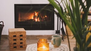 A cozy living room with a fireplace, a small table with a candle, and a television mounted on the wall. - Chão do Ribeirinho, Castelo Branco (Fundao)
