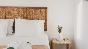 A neatly made bed with white linens and a pink blanket, a wooden headboard with floral carvings, a small wooden nightstand with a vase of dried flowers, and a colorful abstract painting on the wall. - Chão do Ribeirinho, Castelo Branco (Fundao)