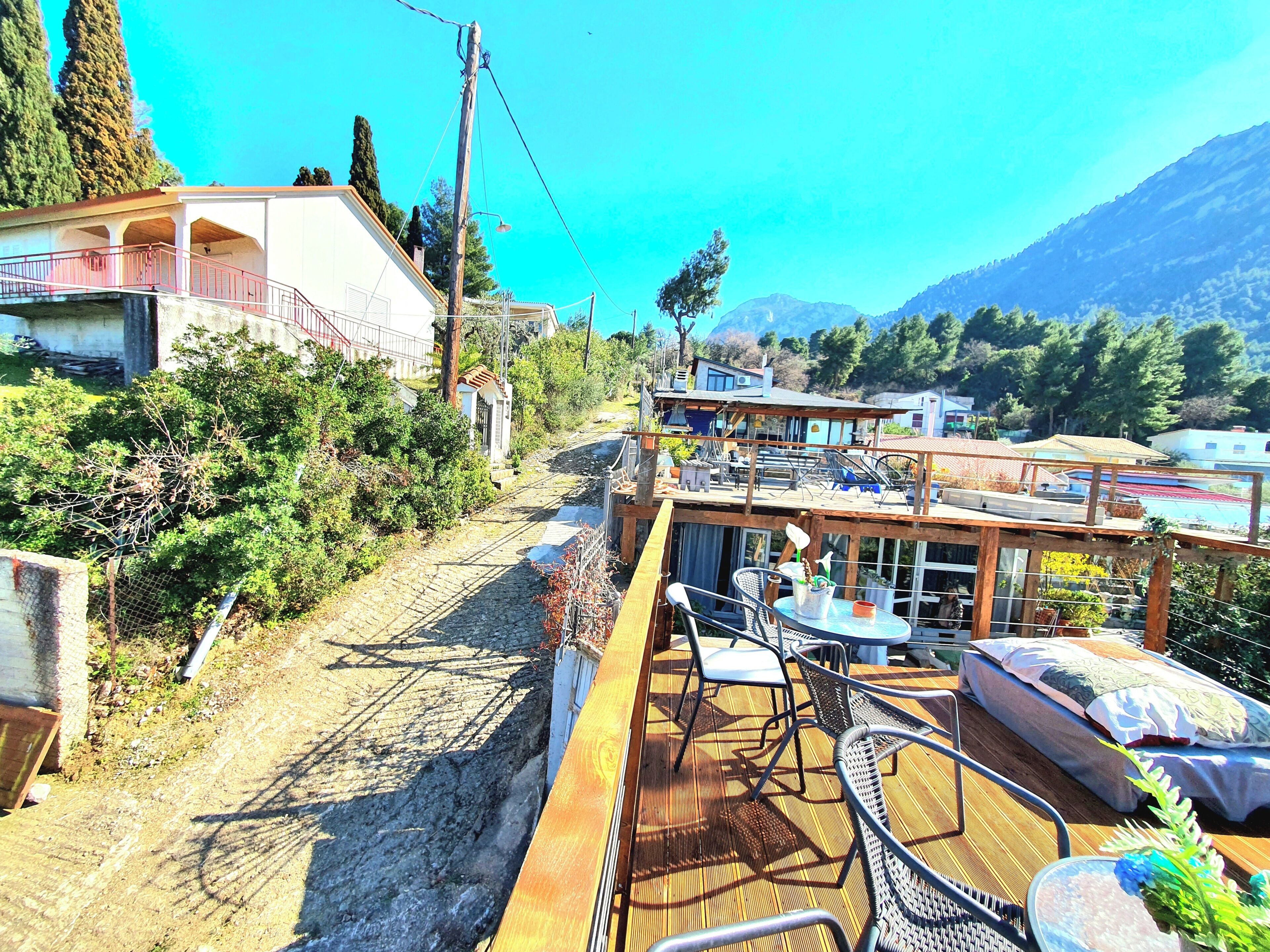 Une terrasse en bois avec des sièges extérieurs, un paysage montagneux en arrière-plan et un bâtiment doté d’un balcon.