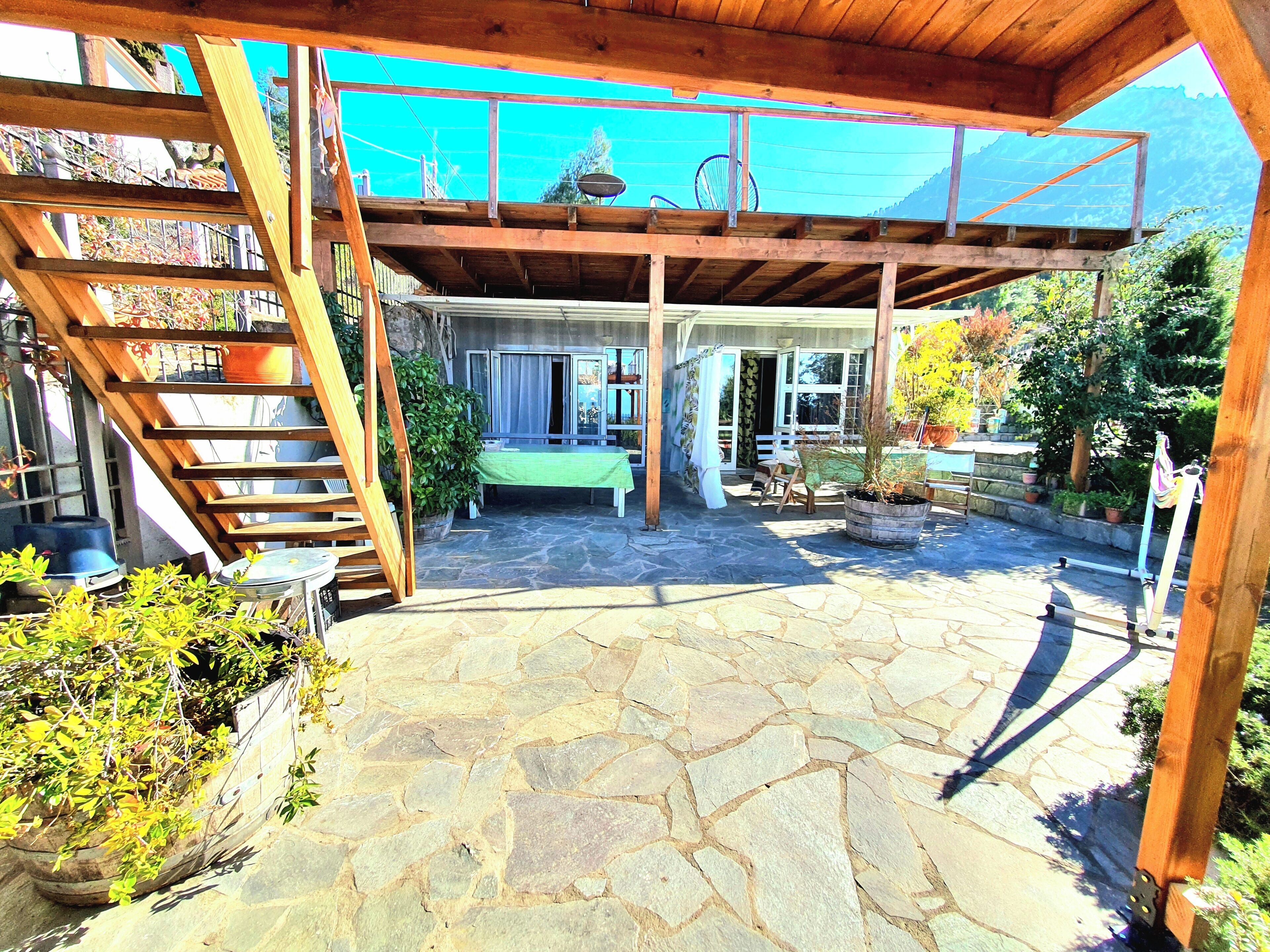 A covered patio with stone flooring, a wooden staircase, and a seating area with a table and chairs.