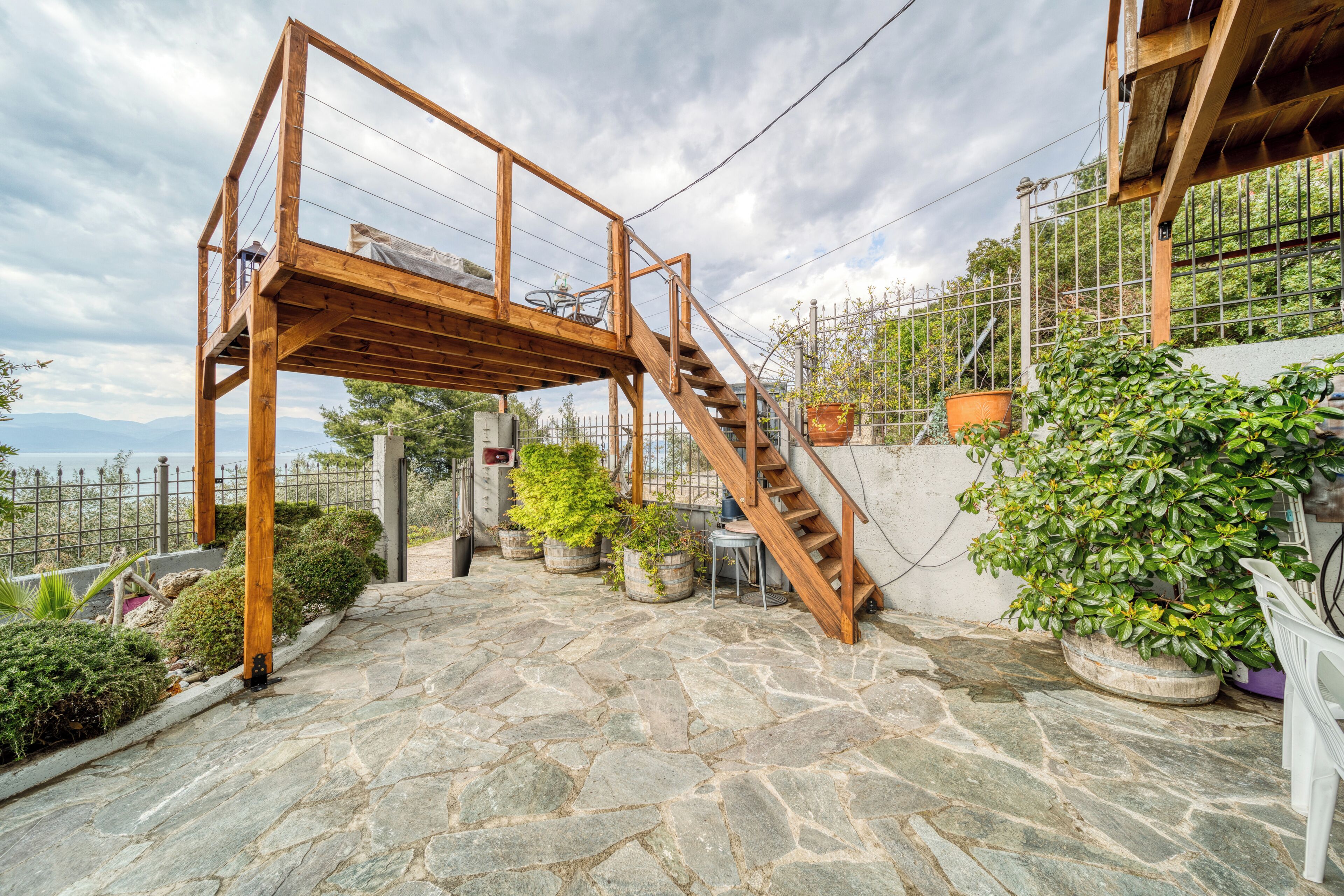 A stone-paved patio with a wooden staircase, potted plants, and a metal fence.