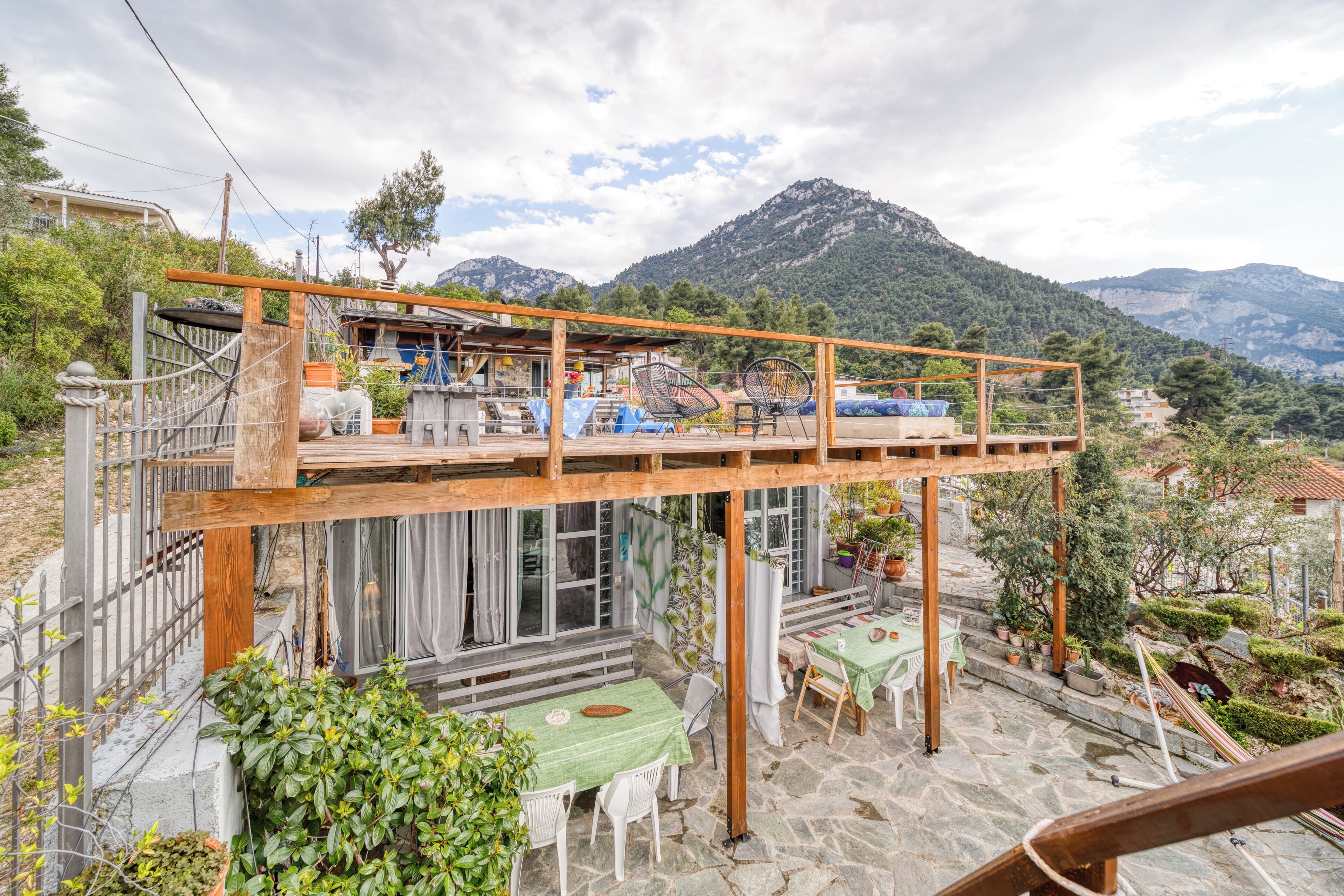 A two-story outdoor patio with stone flooring, wooden pergola, and tables with chairs.
