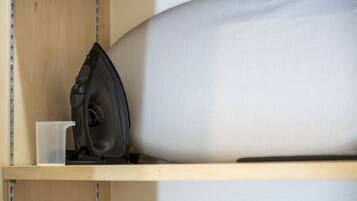 A wooden shelf with a black iron, a clear plastic cup, and a white pillow.
