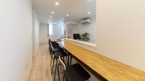 A modern kitchen with a wooden bar and black bar stools, white walls, and recessed lighting.