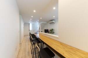 Una cocina moderna con barra de madera y taburetes negros, paredes blancas e iluminación empotrada.