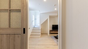 A hallway with a wooden door, a staircase, and a TV in the background.