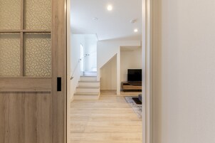 Un pasillo con una puerta de madera, una escalera y un televisor al fondo.