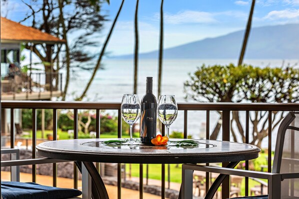 Une table avec une bouteille et deux verres, offrant une vue panoramique sur la mer et les montagnes.
