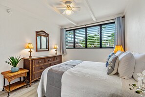 Une chambre à coucher comprenant un lit, des lampes de chevet, une commode, un ventilateur de plafond et une fenêtre avec des stores.
