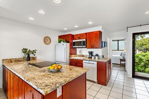 A modern kitchen with granite countertops, wooden cabinets, a microwave, and a sink.