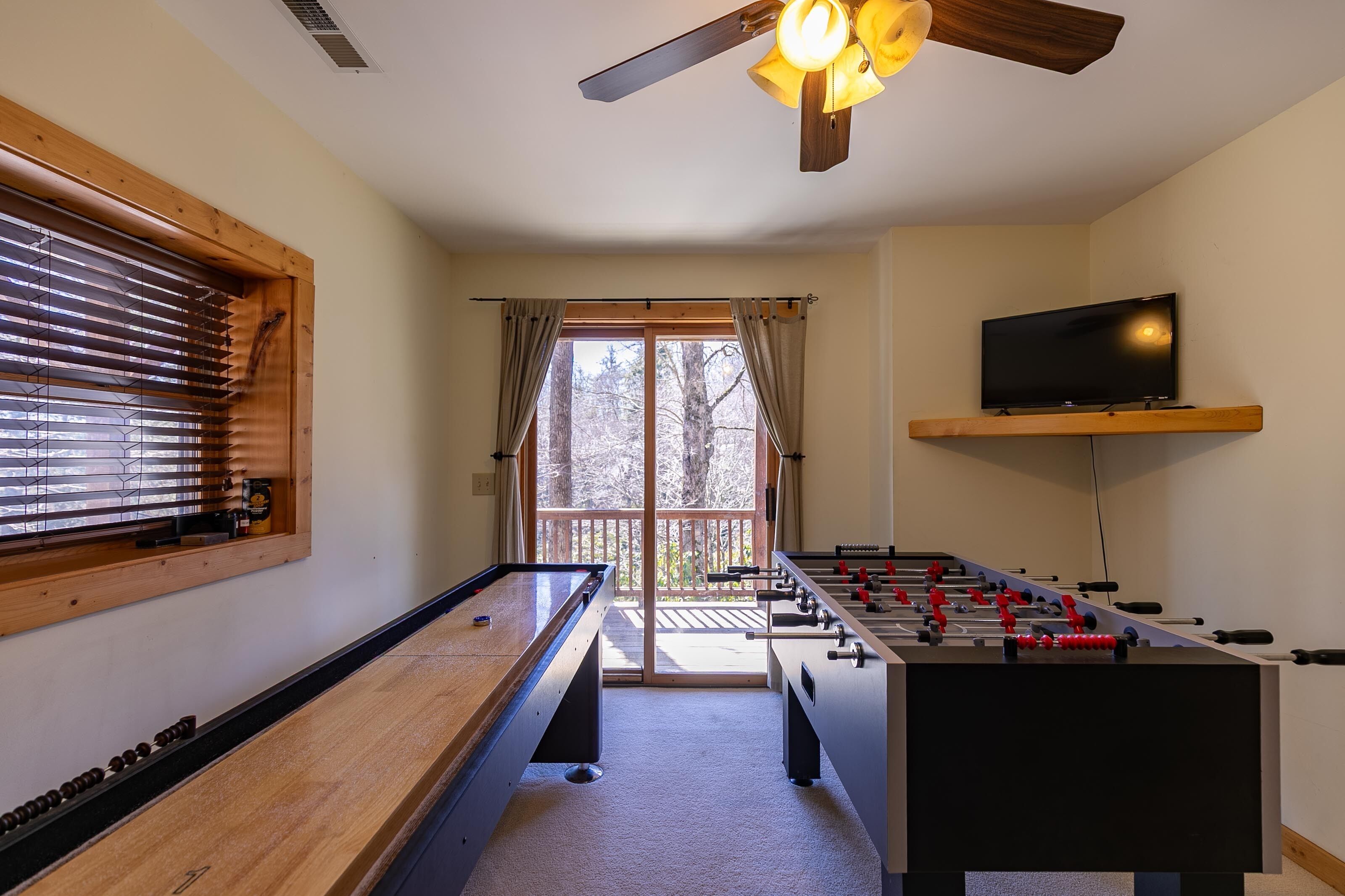 A room with a foosball table, pool table, and a television on a shelf.