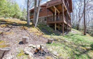 Ein rustikales Blockhaus mit Steinunterbau, Holzoberbau und einem Feuerkorb im Vordergrund.