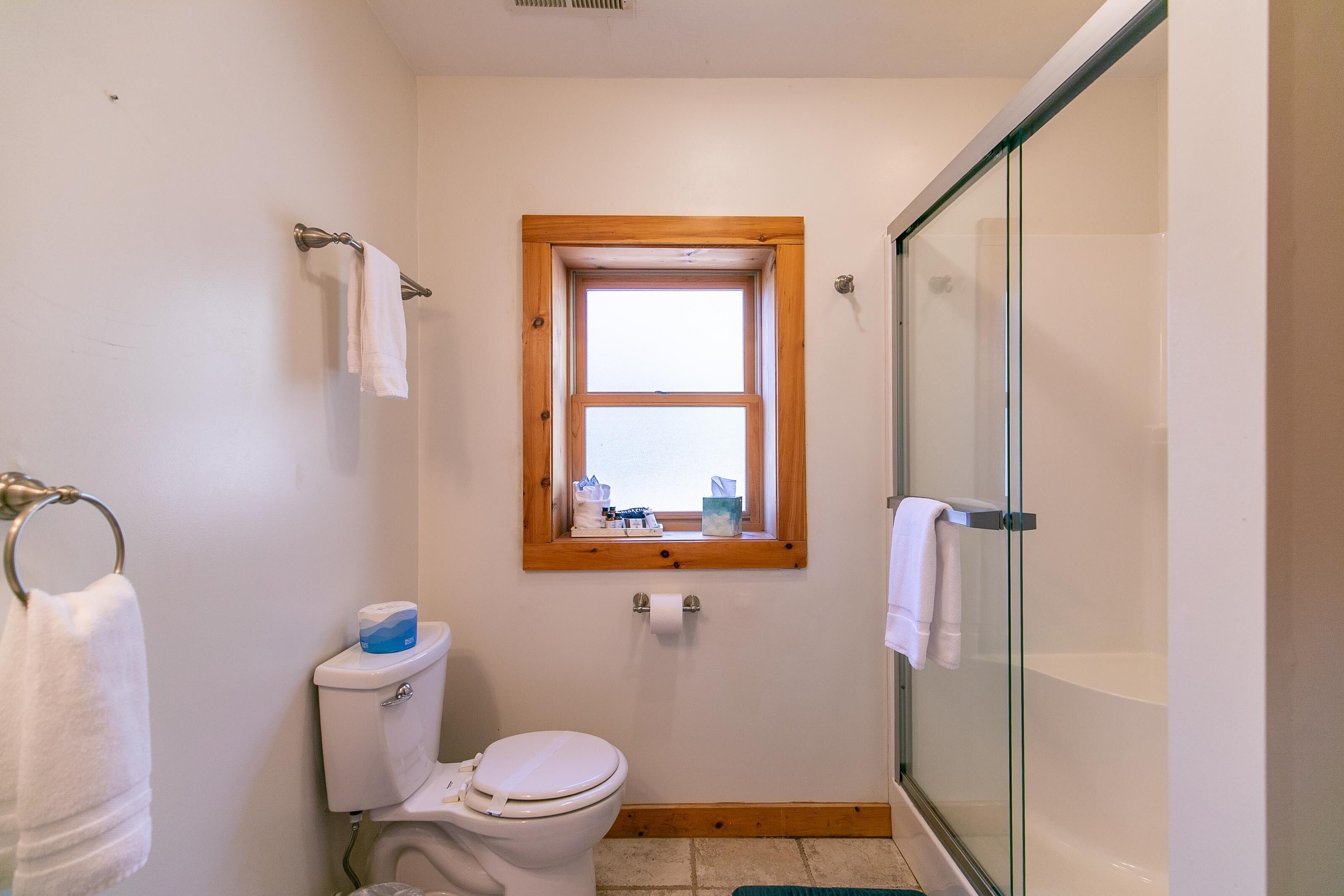 Un bagno con il water, una finestra, box doccia in vetro e porta asciugamani.