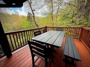 Eine Holzterrasse mit Tisch und Bänken, umgeben von Bäumen.