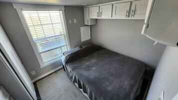A compact bedroom with a bed, a window with blinds, and built-in cabinets.