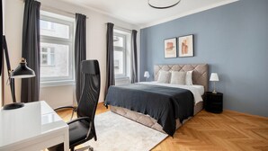 A modern bedroom with a bed, a desk, a chair, and a nightstand.