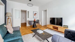 A modern living room with a sofa, coffee table, TV, and a dining area with chairs and a table.