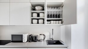 Een moderne keuken met witte kastjes, een magnetron, een koffiezetapparaat en een spoelbak.