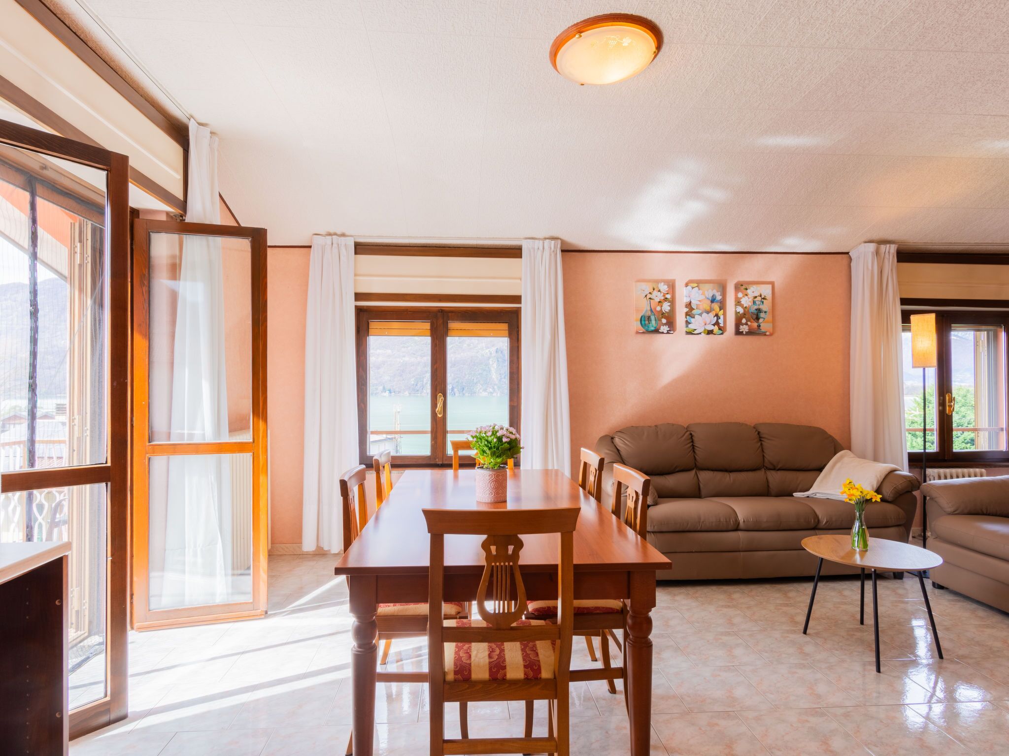 A spacious living area with a dining table, sofa, and a view of a lake through large windows.