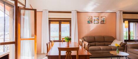 A spacious living area with a dining table, sofa, and a view of a lake through large windows.