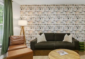 A living room with a sofa, a chair, a coffee table, and a wall covered with a patterned wallpaper.